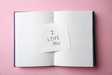 Photo of Piece of paper with phrase I LOVE YOU and notebook on pink background, top view