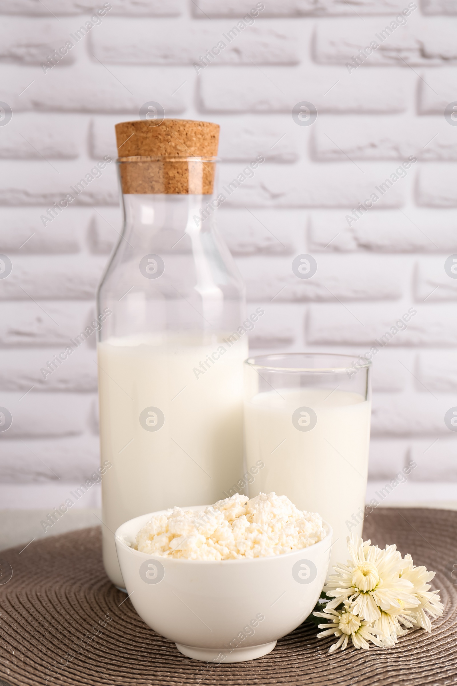 Photo of Tasty fresh milk and cottage cheese on mat against white brick wall