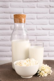 Tasty fresh milk and cottage cheese on mat against white brick wall