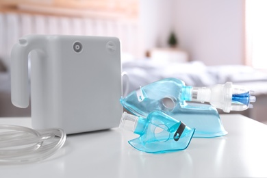 Photo of Modern nebulizer with face masks on white table indoors. Equipment for inhalation