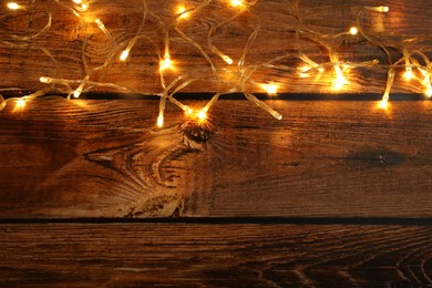 Photo of Glowing festive lights on wooden background, top view. Space for text