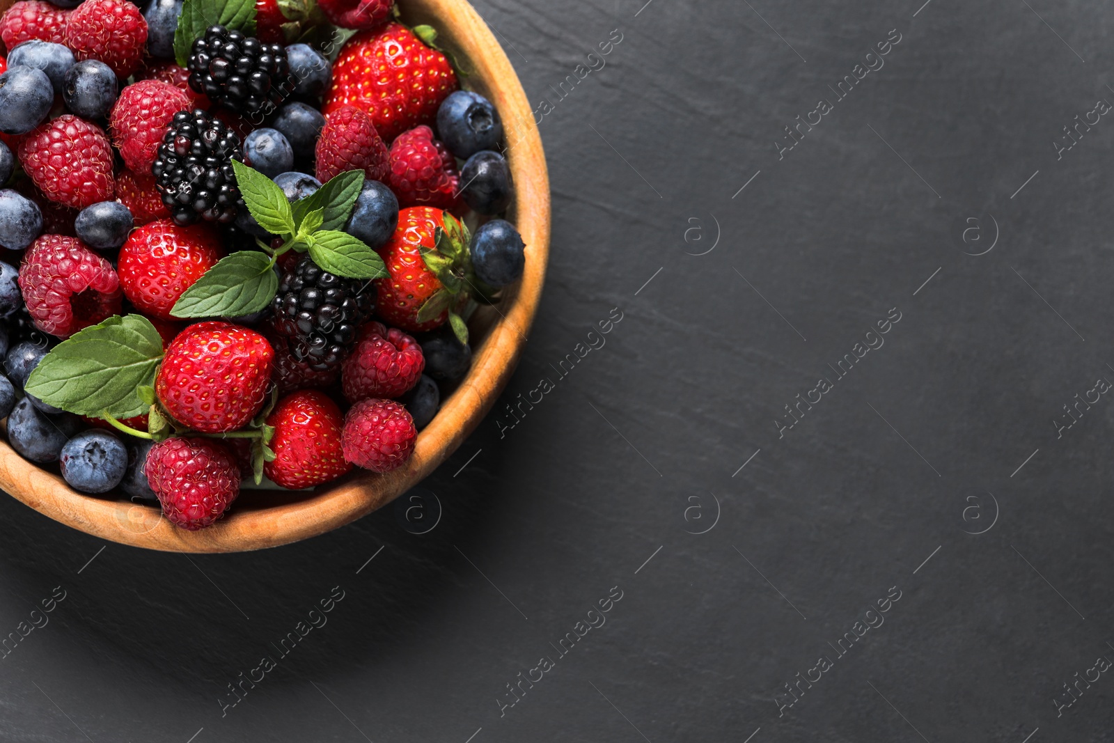 Photo of Many different fresh ripe berries in wooden bowl on black table, top view. Space for text