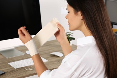Photo of Young woman applying medical bandage onto wrist in office, closeup