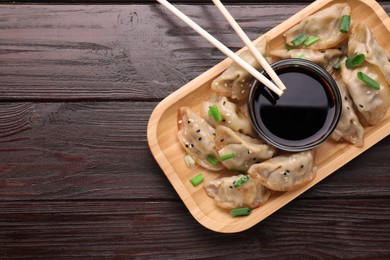 Photo of Delicious gyoza (asian dumplings) with green onions, soy sauce and chopsticks on wooden table, top view. Space for text