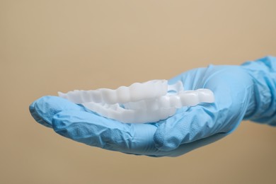Bite correction. Dentist in medical glove holding mouth guards on beige background, closeup