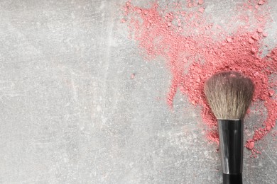 Photo of Makeup brush and scattered blush on grey stone background, top view. Space for text