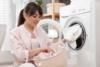 Photo of Happy young housewife putting laundry into washing machine at home