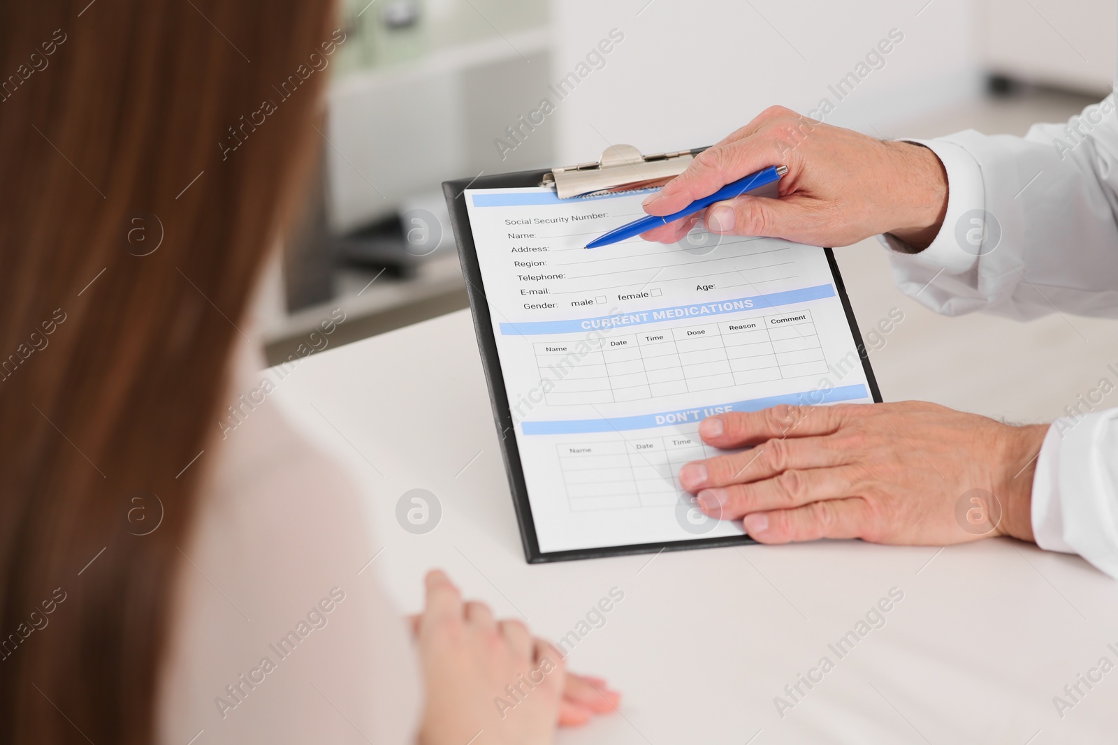 Photo of Doctor showing medical card to patient at table in clinic, closeup