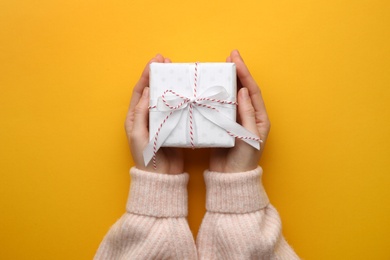 Woman holding Christmas gift box on orange background, top view