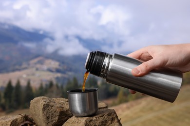 Photo of Woman pouring hot instant coffee from thermos in mountains, closeup
