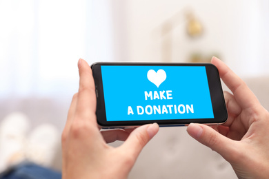 Image of Woman holding smartphone with text MAKE A DONATION indoors, closeup