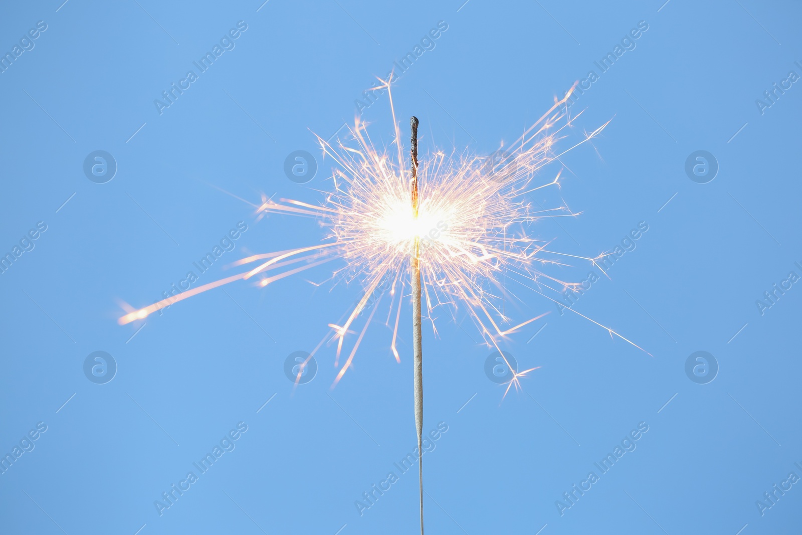 Photo of Bright burning sparkler on light blue background, closeup