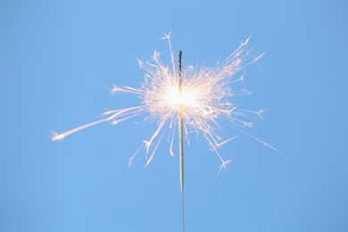 Photo of Bright burning sparkler on light blue background, closeup