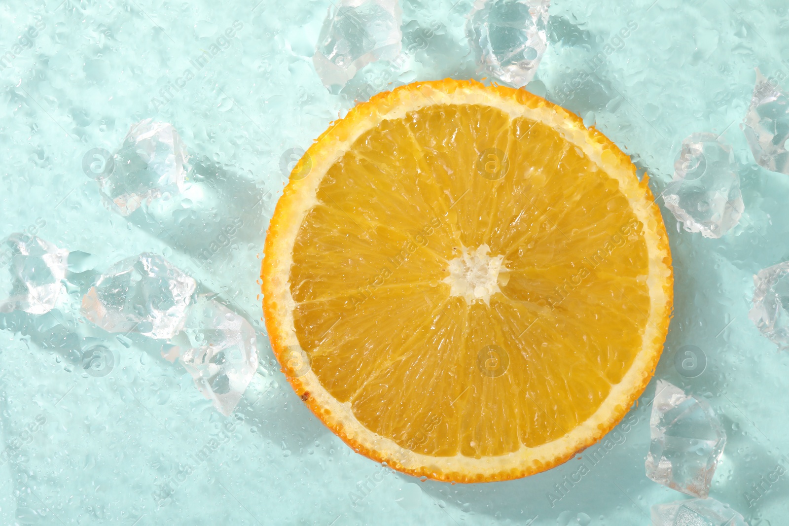 Photo of Slice of juicy orange and ice cubes on light blue background, top view