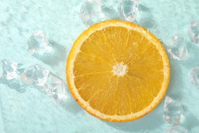 Slice of juicy orange and ice cubes on light blue background, top view