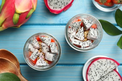 Photo of Granola with strawberries and pitahaya in glass jars on light blue wooden table, top view