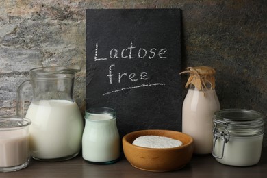 Dairy products and board with phrase Lactose Free on wooden table near grey wall