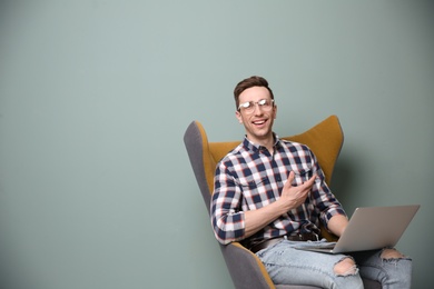 Young blogger with laptop sitting in armchair against color wall