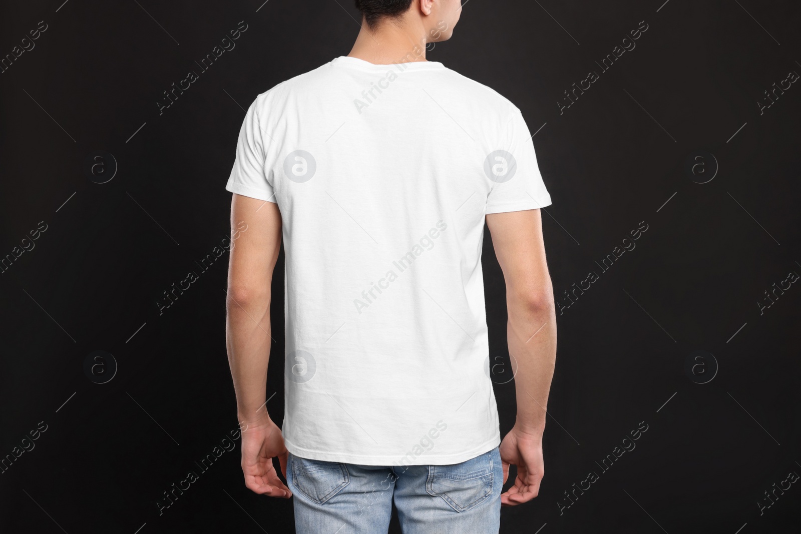 Photo of Man wearing white t-shirt on black background, back view. Mockup for design