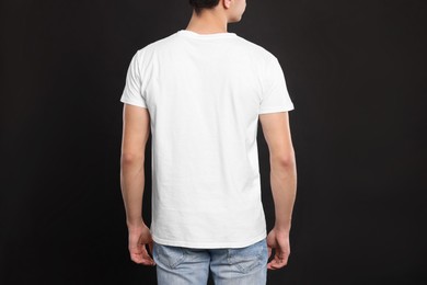 Man wearing white t-shirt on black background, back view. Mockup for design