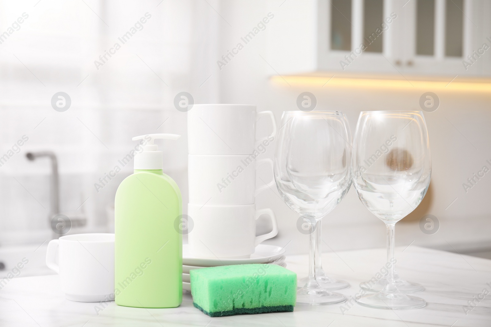 Photo of Clean glasses, cups and cleaning product on table in stylish kitchen