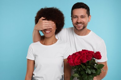 International dating. Handsome man presenting roses to his beloved woman on light blue background