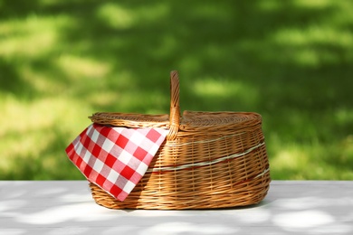 Photo of Wicker basket with blanket on table in park. Summer picnic