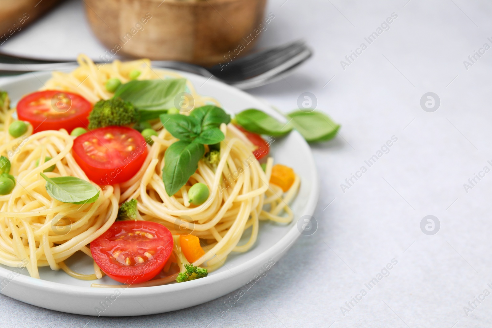 Photo of Plate of delicious pasta primavera and cutlery on light gray table, closeup. Space for text