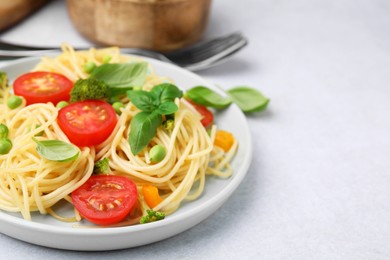 Plate of delicious pasta primavera and cutlery on light gray table, closeup. Space for text