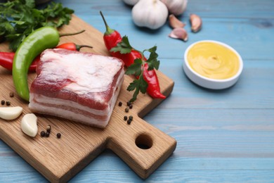 Photo of Piece of pork fatback with garlic and chilli pepper on light blue wooden table