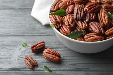 Photo of Dish with tasty pecan nuts on wooden table, closeup