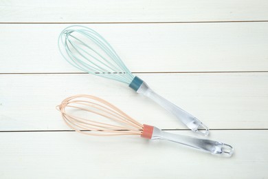 Two whisks on white wooden table, top view