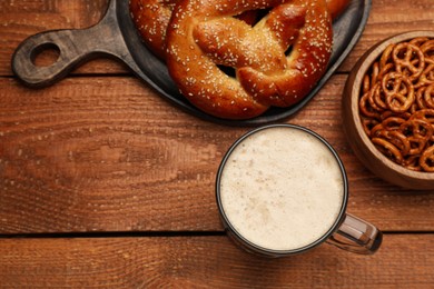 Tasty freshly baked pretzels, crackers and mug of beer on wooden table, flat lay. Space for text