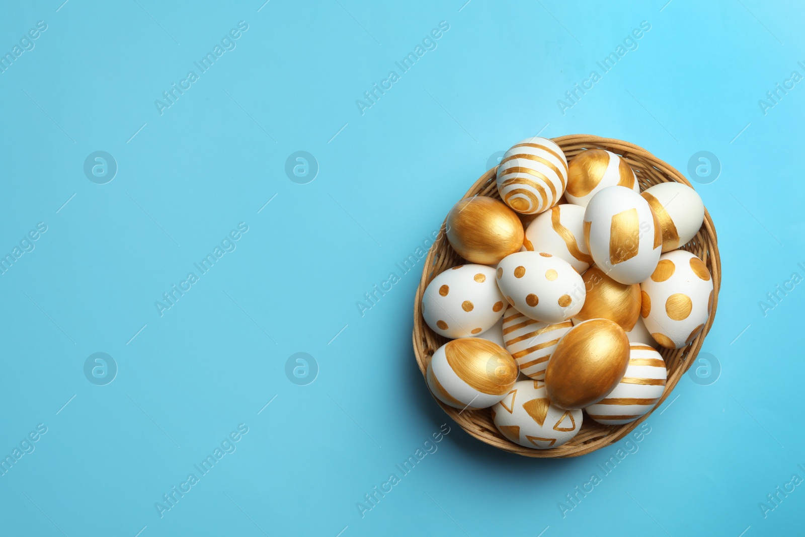 Photo of Wicker basket of traditional Easter eggs decorated with golden paint on color background, top view. Space for text