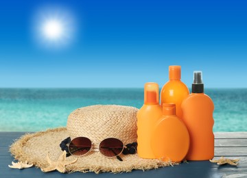 Image of Different bottles of skin sun protection products and beach accessories on blue wooden table against seascape. Space for design