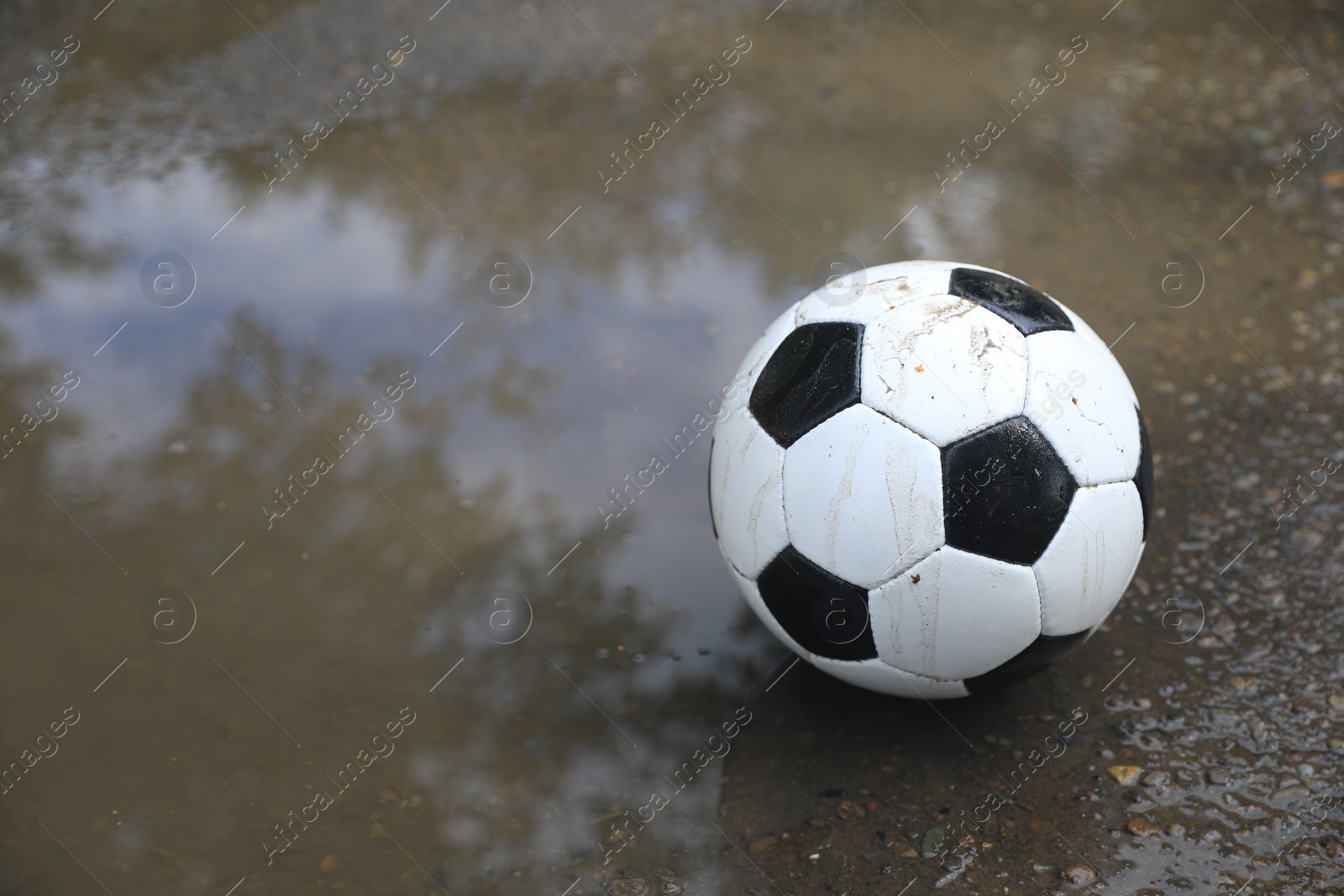 Photo of Soccer ball near puddle outdoors, space for text