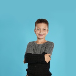 Photo of Cute little boy in warm sweater on blue background, space for text. Winter season