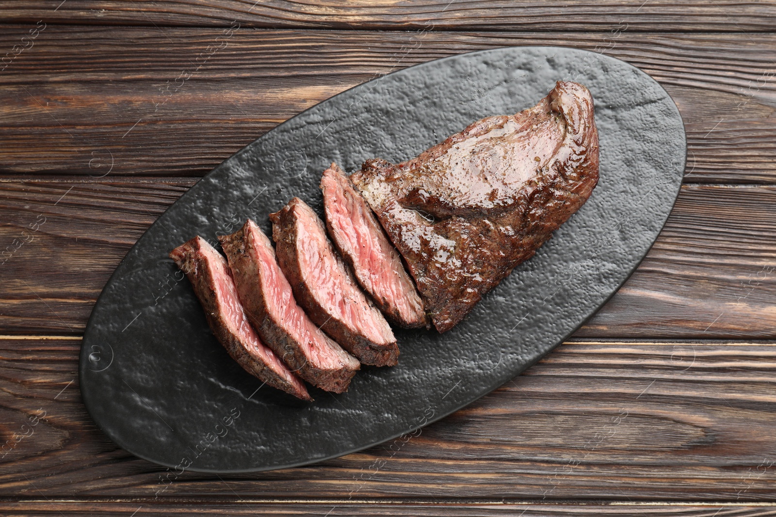 Photo of Pieces of delicious grilled beef meat on wooden table, top view