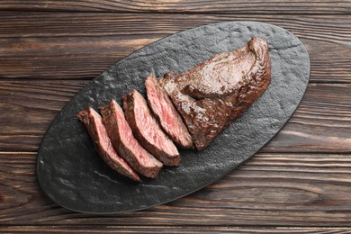 Photo of Pieces of delicious grilled beef meat on wooden table, top view