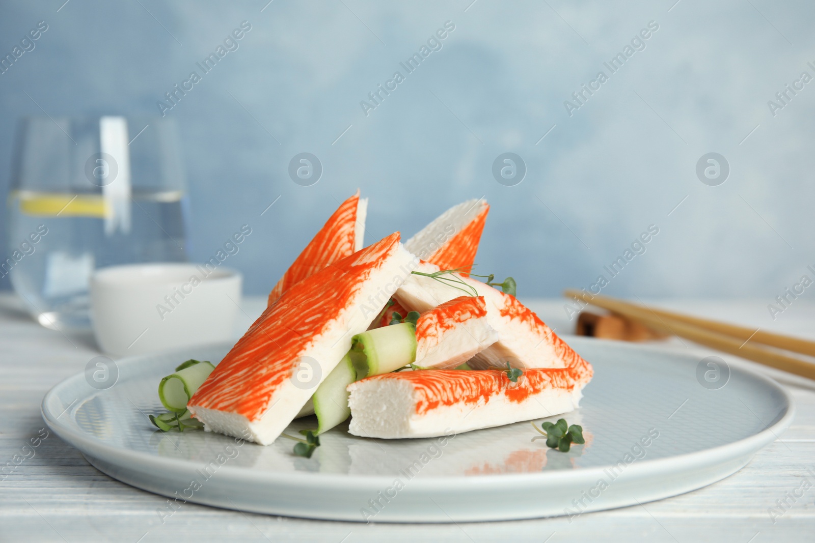 Photo of Fresh crab sticks with cucumber served on white wooden table, closeup