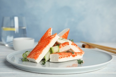 Photo of Fresh crab sticks with cucumber served on white wooden table, closeup