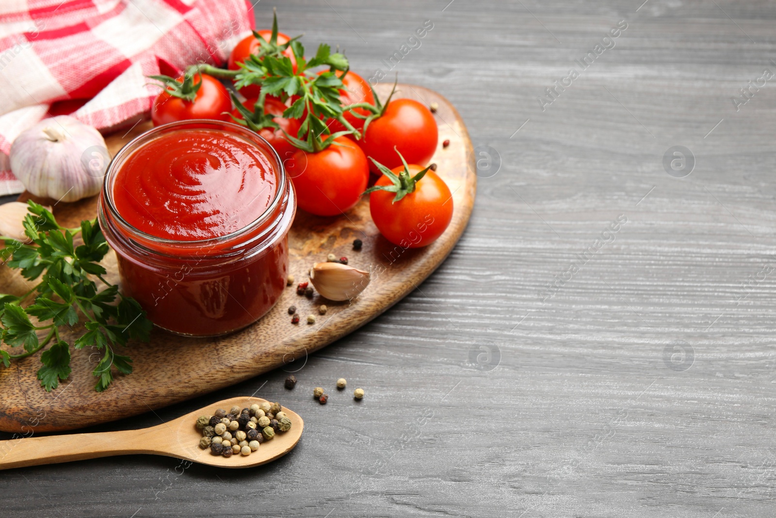 Photo of Tasty ketchup, fresh tomatoes, parsley and spices on grey wooden table, space for text