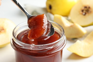 Photo of Taking tasty homemade quince jam from jar at table, closeup