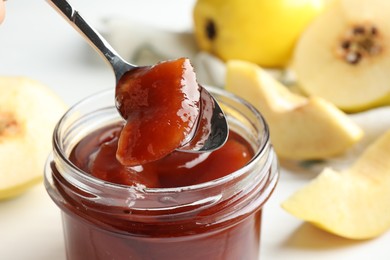 Taking tasty homemade quince jam from jar at table, closeup