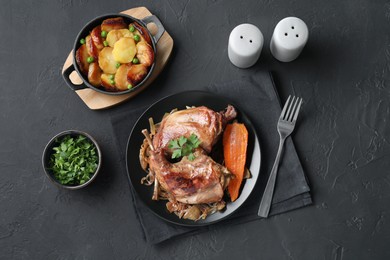 Photo of Tasty cooked rabbit meat with vegetables and potato served on black table, flat lay