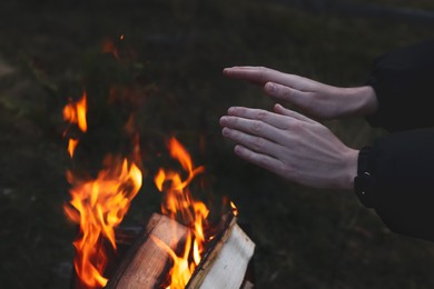 Photo of Tourist warming hands near bonfire outdoors in evening, closeup
