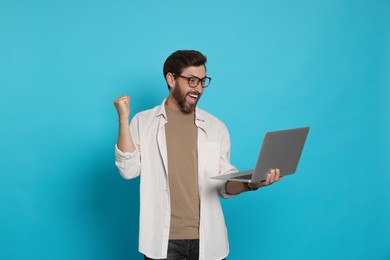 Emotional man with laptop on light blue background