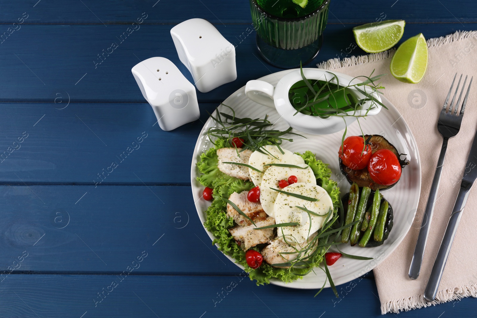 Photo of Delicious mozzarella, chicken and vegetables with tarragon served on blue wooden table, above view. Space for text