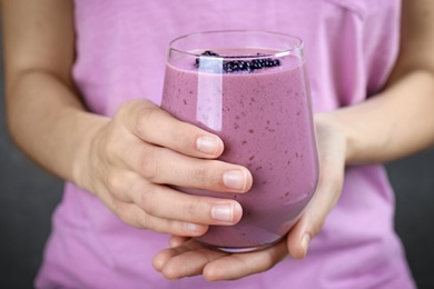 Young woman holding glass of tasty blackberry smoothie, closeup