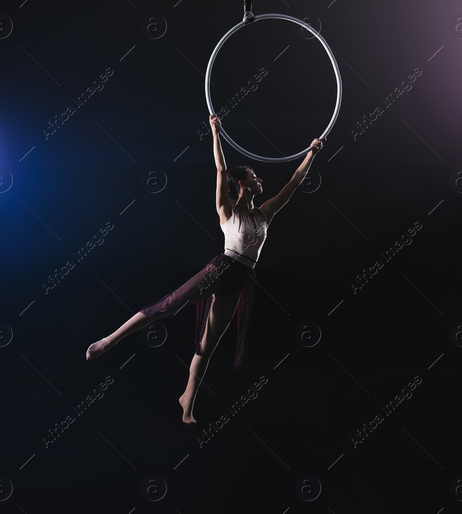 Photo of Young woman performing acrobatic element on aerial ring indoors